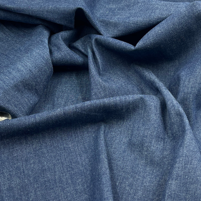 A close-up of draped blue fabric with a fine textured weave, showing soft folds and shadows.
