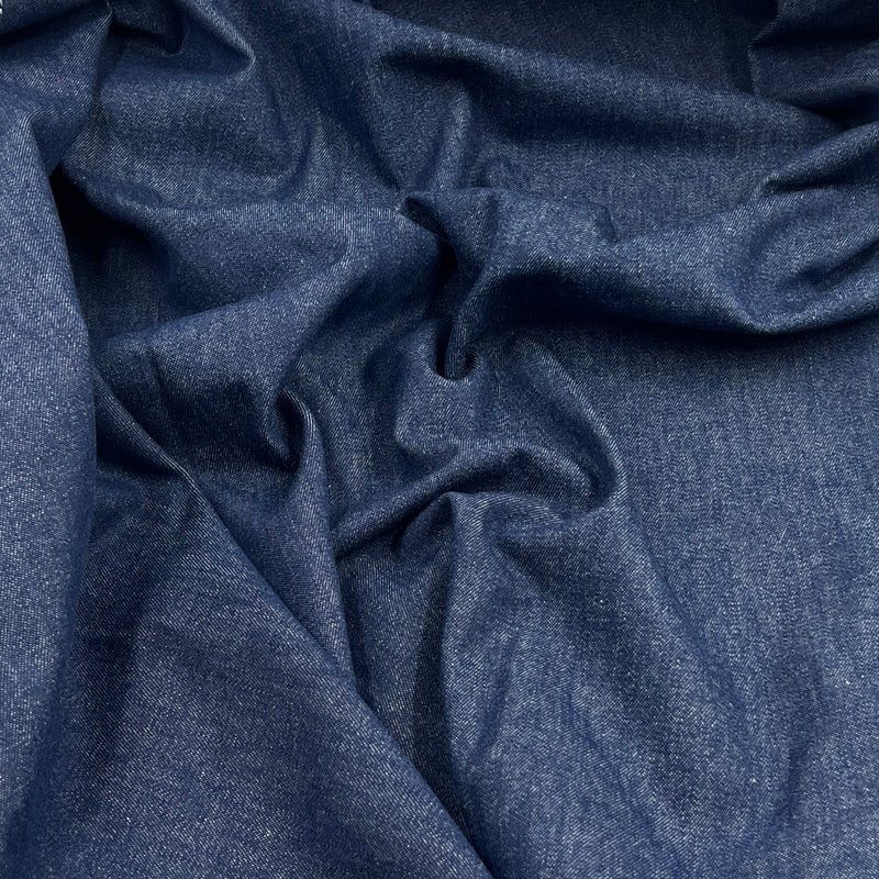 A close-up of draped dark blue fabric with a fine textured weave, showing soft folds and shadows.