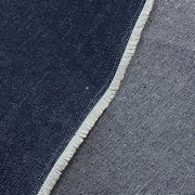 Close-up of a woven textile surface showing a dark indigo blue area on the left and a lighter heather gray-blue area on the right, divided by a frayed white edge.