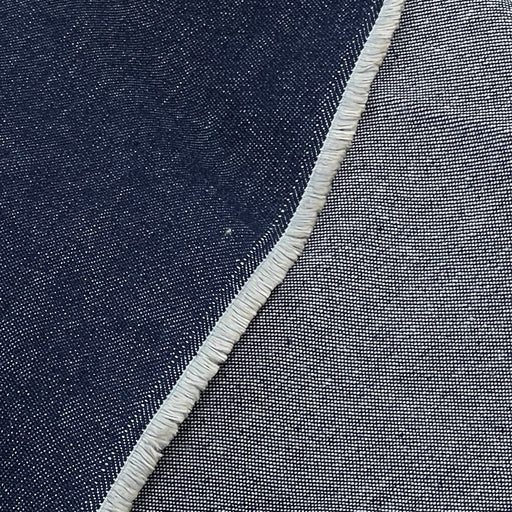 Close-up of a woven textile surface showing a dark indigo blue area on the left and a lighter heather gray-blue area on the right, divided by a frayed white edge.
