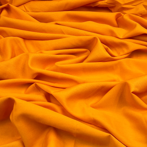 Bright orange fabric draped in soft folds, showing a smooth texture and rich color.