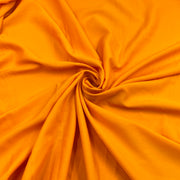 Bright orange rayon challis fabric draped in a spiral swirl pattern, showing its smooth texture and soft folds.