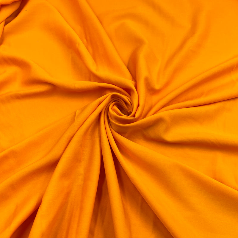 Bright orange rayon challis fabric draped in a spiral swirl pattern, showing its smooth texture and soft folds.