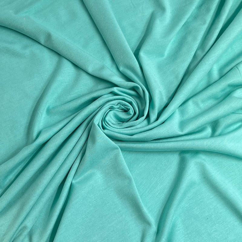 A close-up of mint green or aqua fabric arranged in a spiral drape, showing the material texture and color.