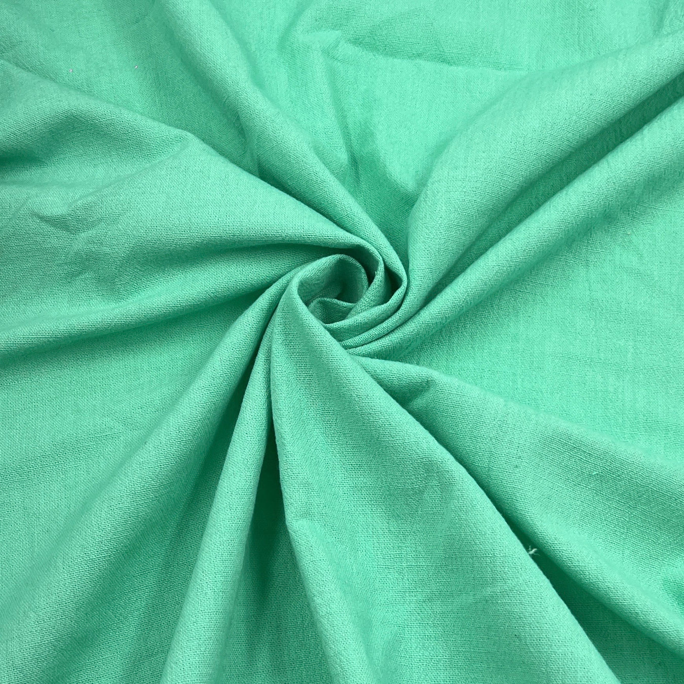 A close-up of mint green fabric arranged in a spiral drape, showing the material texture and color.