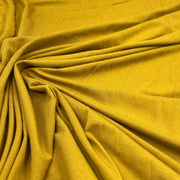 A close-up of draped mustard yellow fabric with a visible woven texture, arranged in soft folds and swirls.