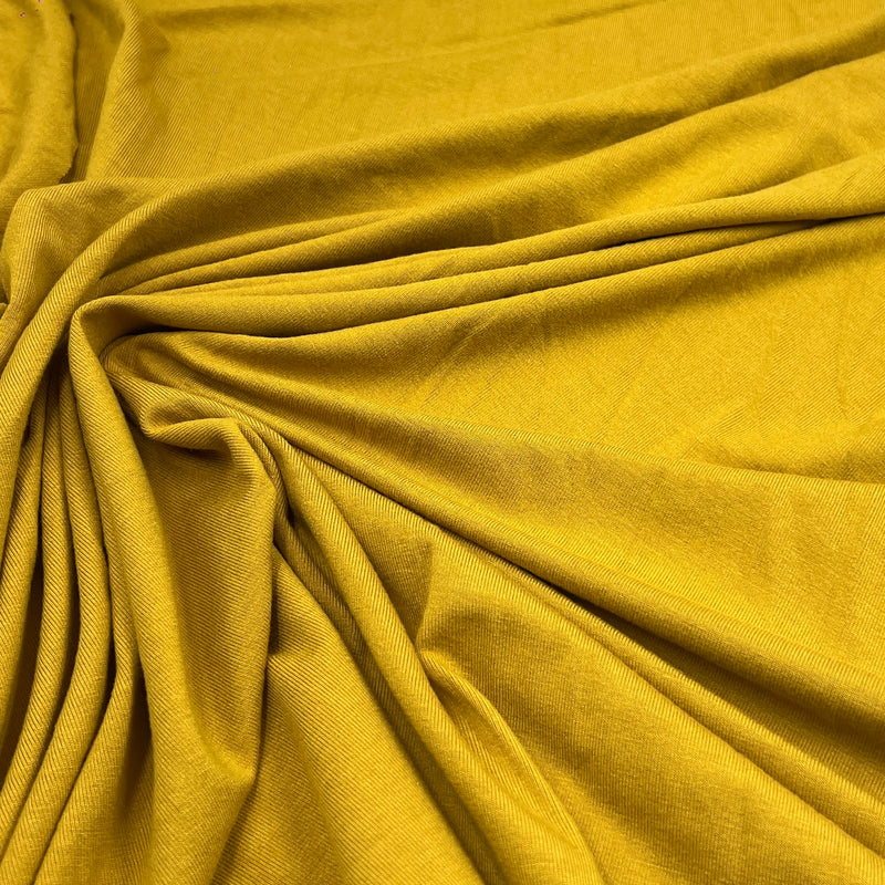 A close-up of draped mustard yellow fabric with a visible woven texture, arranged in soft folds and swirls.