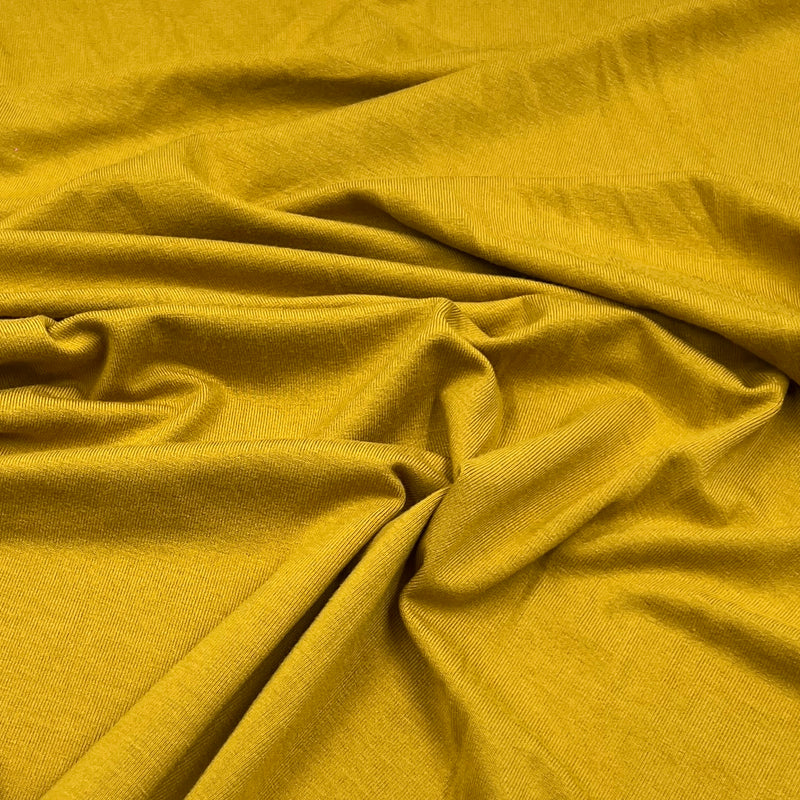 A close-up of draped mustard yellow fabric with a fine textured weave, showing soft folds and shadows.