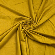 A close-up of draped mustard yellow fabric arranged in a spiral pattern, showing its soft texture and color.