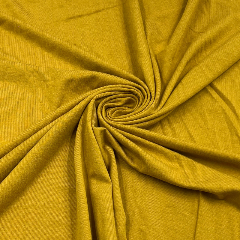 A close-up of draped mustard yellow fabric arranged in a spiral pattern, showing its soft texture and color.