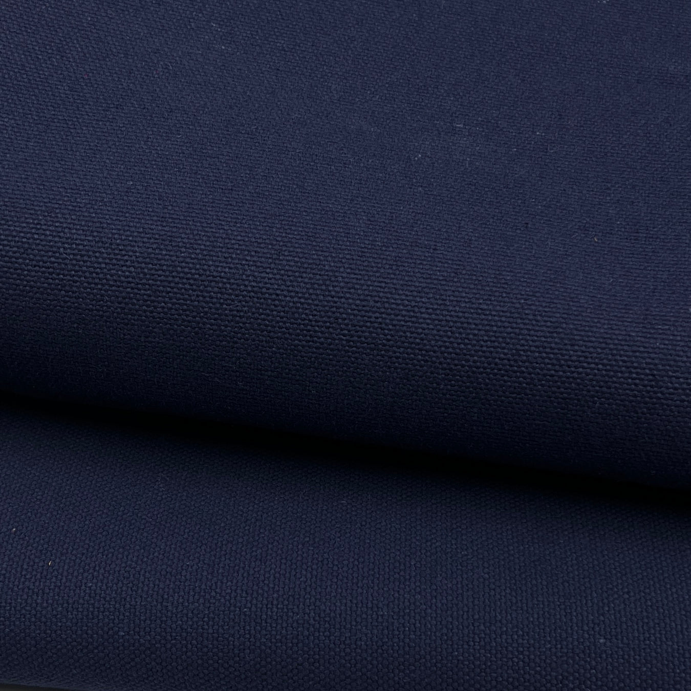 A close-up of dark navy blue canvas fabric with a visible woven texture, shown in two folded layers.