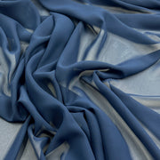 A close-up of draped blue fabric with soft folds and a subtle sheen, filling the frame against a matching light blue background.