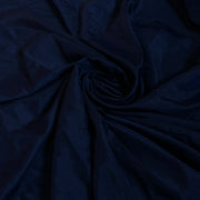 A close-up of dark navy blue fabric with a subtle sheen, arranged in a spiral drape pattern.