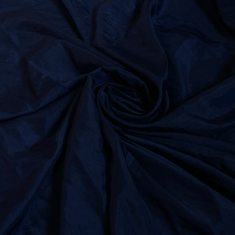 A close-up of dark navy blue fabric with a subtle sheen, arranged in a spiral drape pattern.