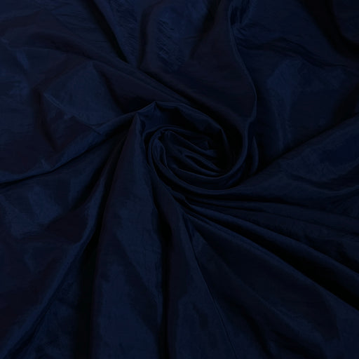 A close-up of dark navy blue fabric with a subtle sheen, arranged in a spiral drape pattern.