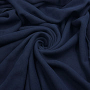 A close-up of draped navy blue fabric arranged in a spiral pattern, showing its soft texture and folds.