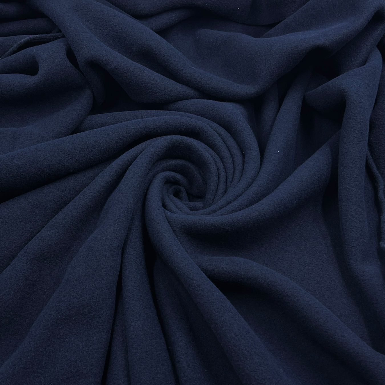 A close-up of draped navy blue fabric arranged in a spiral pattern, showing its soft texture and folds.