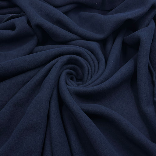 A close-up of draped navy blue fabric arranged in a spiral pattern, showing its soft texture and folds.