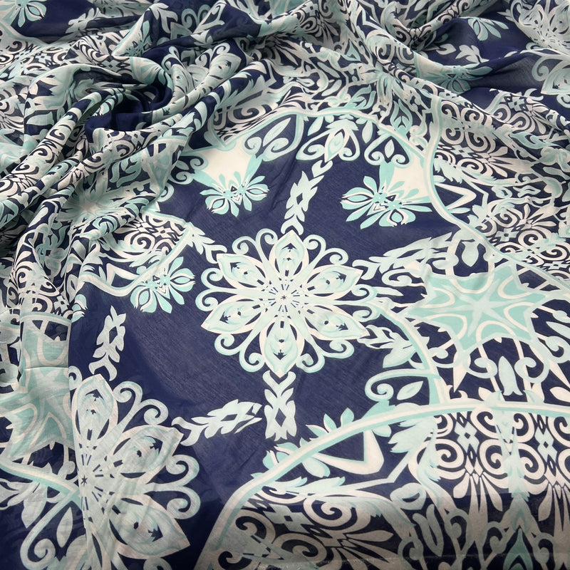 A close-up of draped fabric featuring an intricate floral and scroll pattern in light aqua, white, and navy blue.