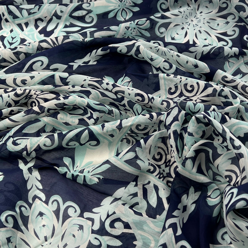 A close-up of draped fabric with an allover floral and scroll pattern in navy blue, pale mint green, and white.