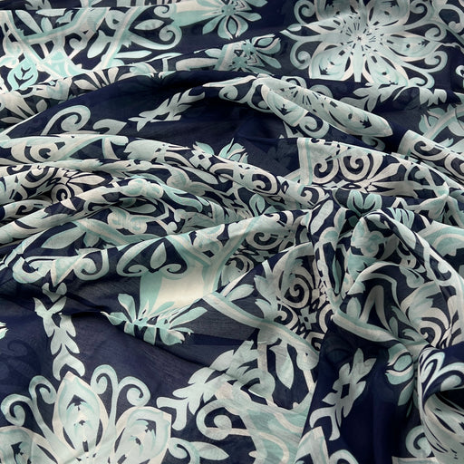 A close-up of draped fabric with an allover floral and scroll pattern in navy blue, pale mint green, and white.
