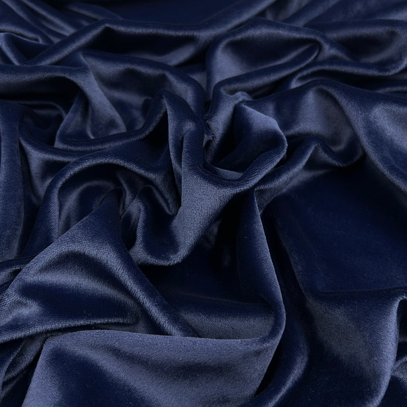 A close-up of draped navy blue velour fabric with soft folds and a subtle sheen.