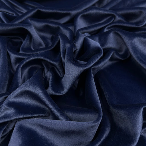 A close-up of draped navy blue velour fabric with soft folds and a subtle sheen.
