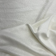 A close-up of a soft, textured off-white fabric with a smooth, slightly lustrous fold running diagonally across the frame.