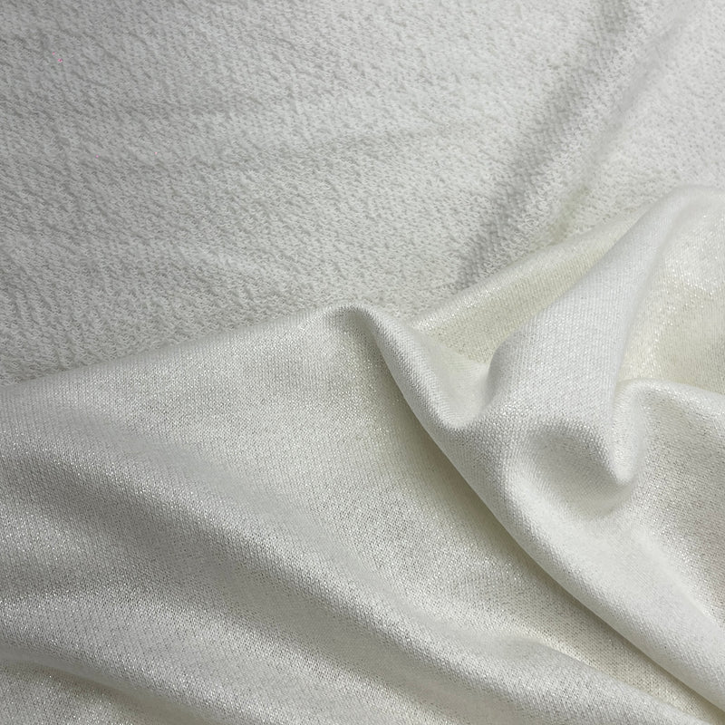 A close-up of a soft, textured off-white fabric with a smooth, slightly lustrous fold running diagonally across the frame.