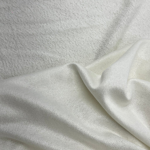 A close-up of a soft, textured off-white fabric with a smooth, slightly lustrous fold running diagonally across the frame.