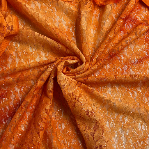 Close-up of orange lace fabric with a floral pattern, arranged in a spiral drape to show texture and transparency.