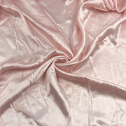 A close-up of draped satin fabric in a soft blush pink color, showing its smooth texture and sheen.