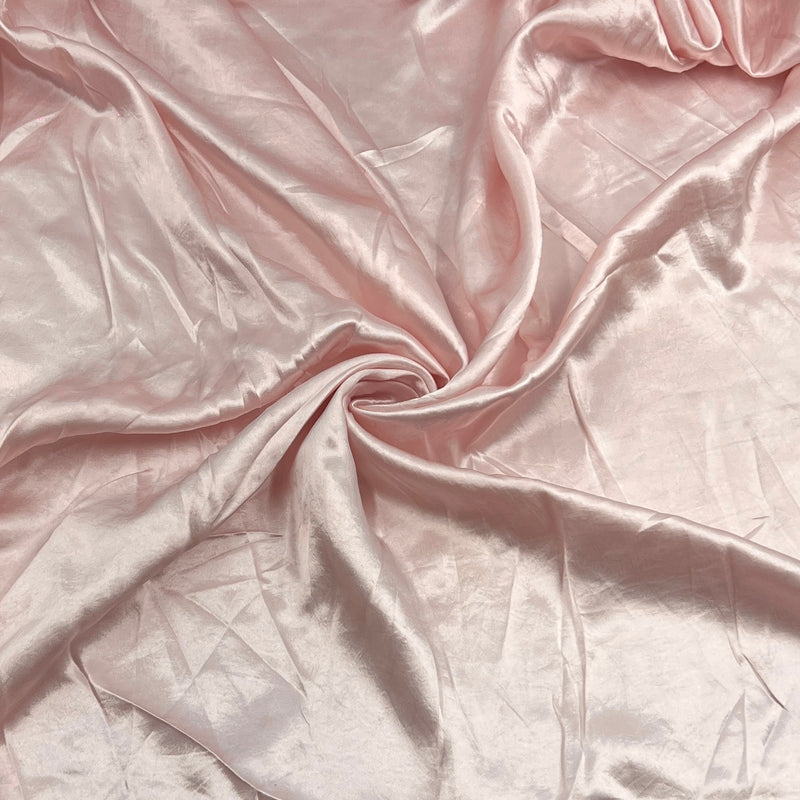 A close-up of draped satin fabric in a soft blush pink color, showing its smooth texture and sheen.