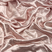 Draped satin fabric in a soft blush pink color, showing its smooth texture and elegant sheen with elegant folds.
