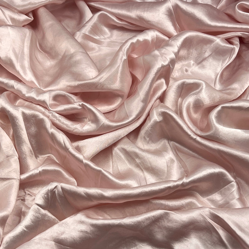 Draped satin fabric in a soft blush pink color, showing its smooth texture and elegant sheen with elegant folds.