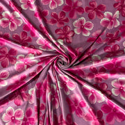A close-up of a draped fabric with a pink and magenta floral pattern, arranged in a spiral twist to show its texture and sheen.