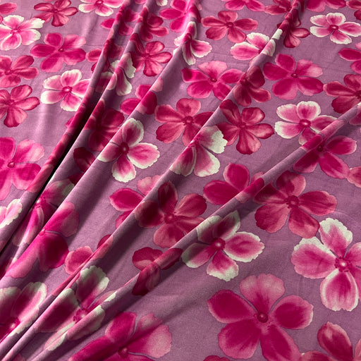 A close-up of draped fabric with a pink and magenta floral print on a mauve-purple background.
