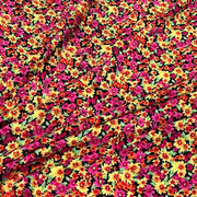 A close-up of a vibrant floral fabric featuring a dense pattern of small daisy-like flowers in magenta pink, bright yellow, orange, and green on a black background.