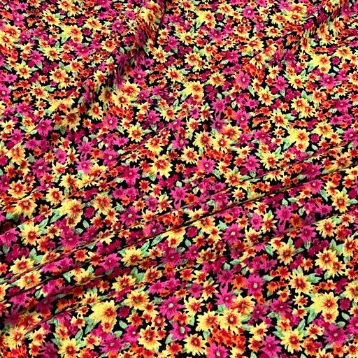 A close-up of a vibrant floral fabric featuring a dense pattern of small daisy-like flowers in magenta pink, bright yellow, orange, and green on a black background.