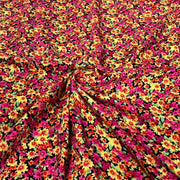A close-up of a draped fabric with a dense, all-over floral print featuring bright pink, yellow, orange, and green flowers on a black background.