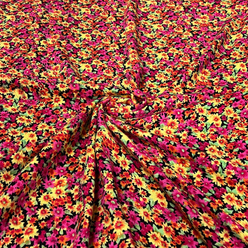 A close-up of a draped fabric with a dense, all-over floral print featuring bright pink, yellow, orange, and green flowers on a black background.