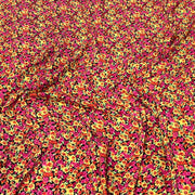 A close-up of a fabric surface with an all-over dense floral print in bright pink, yellow, orange, and small green accents on a dark background.
