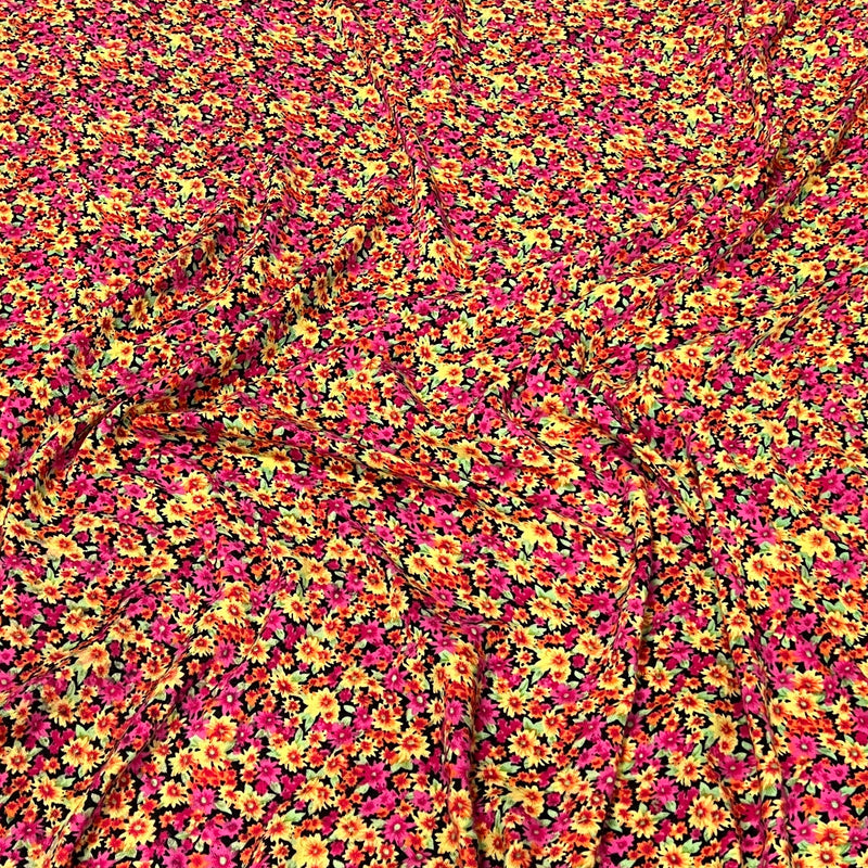 A close-up of a fabric surface with an all-over dense floral print in bright pink, yellow, orange, and small green accents on a dark background.