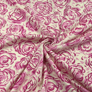 A close-up of draped fabric featuring a pink watercolor-style rose pattern on a warm cream background.
