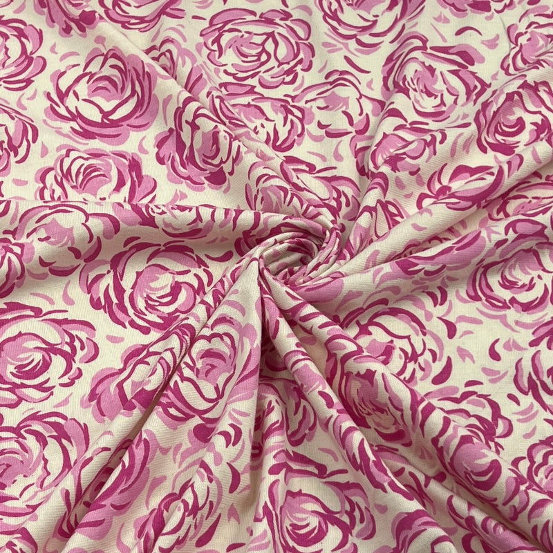 A close-up of draped fabric featuring a pink watercolor-style rose pattern on a warm cream background.