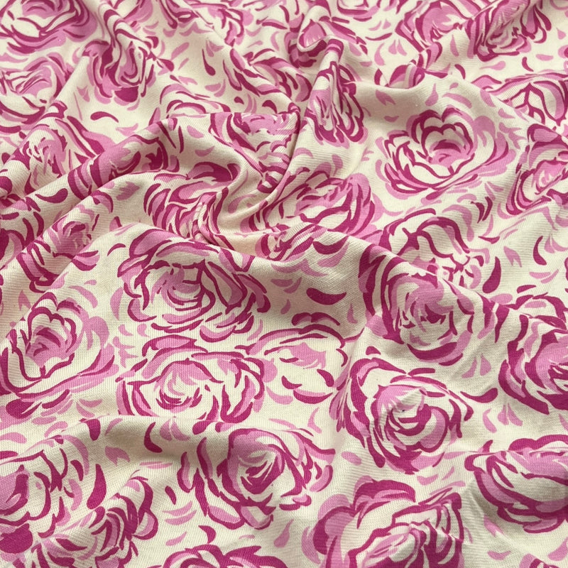 A close-up of draped fabric featuring a repeating pink rose print on a warm off-white background.