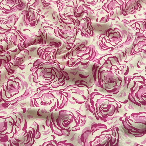A close-up of draped fabric featuring a repeating pink rose print on a warm off-white background.