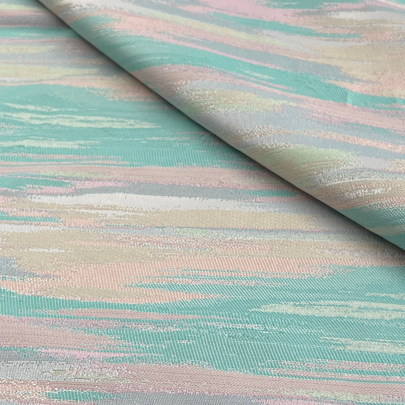 A close-up of a draped fabric with a textured, woven pattern featuring horizontal brushstroke-like bands of mint green, dusty pink, pale blue, and cream.