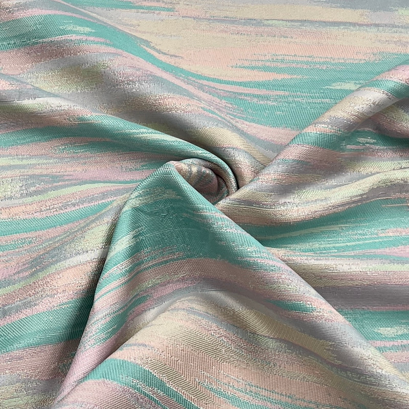 A close-up of draped fabric with an abstract brushstroke pattern in soft mint green, blush pink, and warm beige tones.