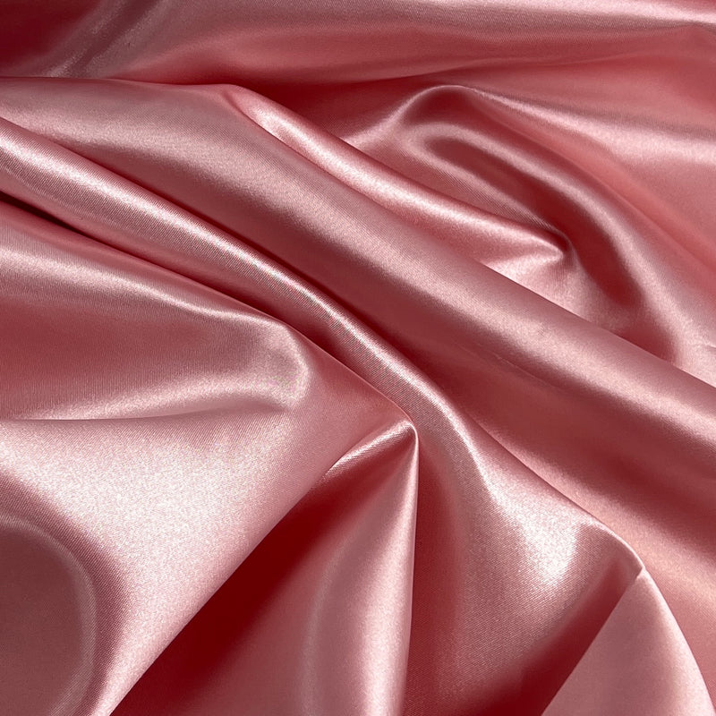 A close-up of draped satin fabric in a soft dusty pink color, showing the smooth sheen and folds of the material.